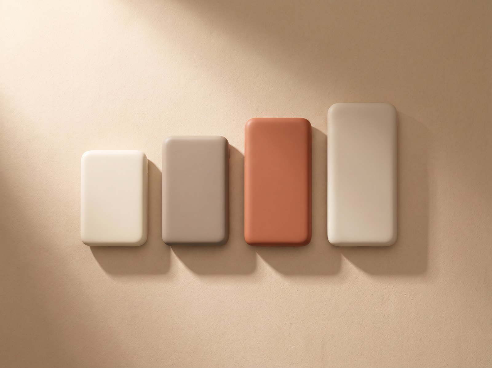Four portable power banks of different sizes laid out on a warm studio surface